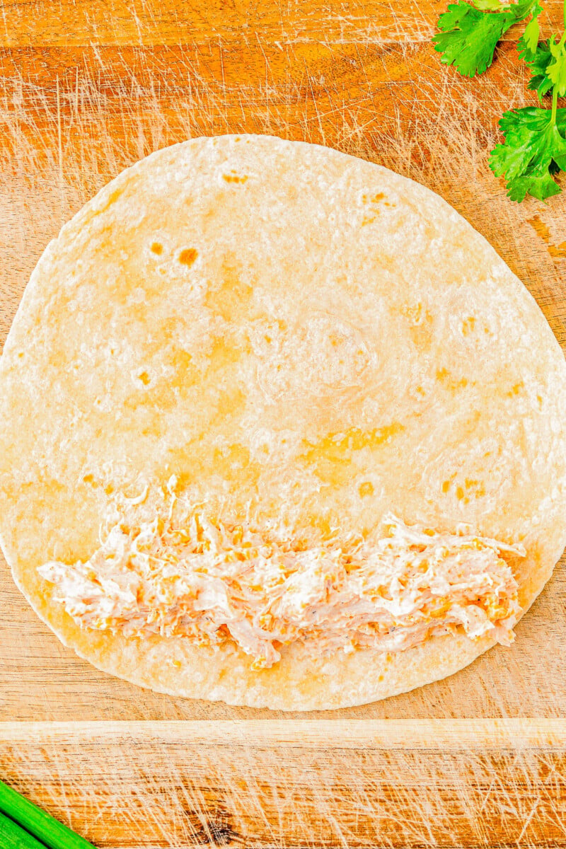 A single flour tortilla on a wooden cutting board, with fresh cilantro and green onions nearby.