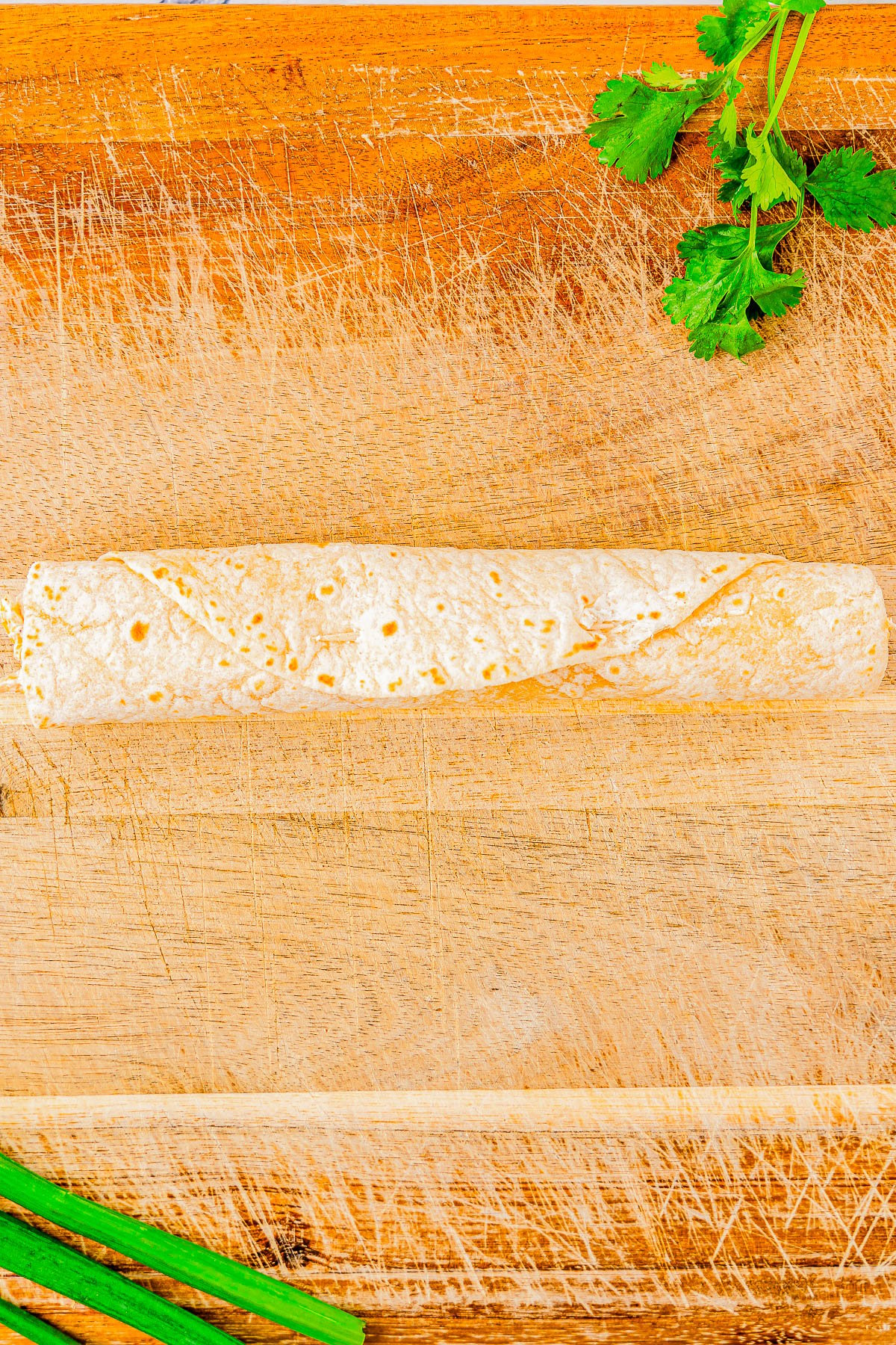 A single taquito on a wooden cutting board, garnished with cilantro and green onions.
