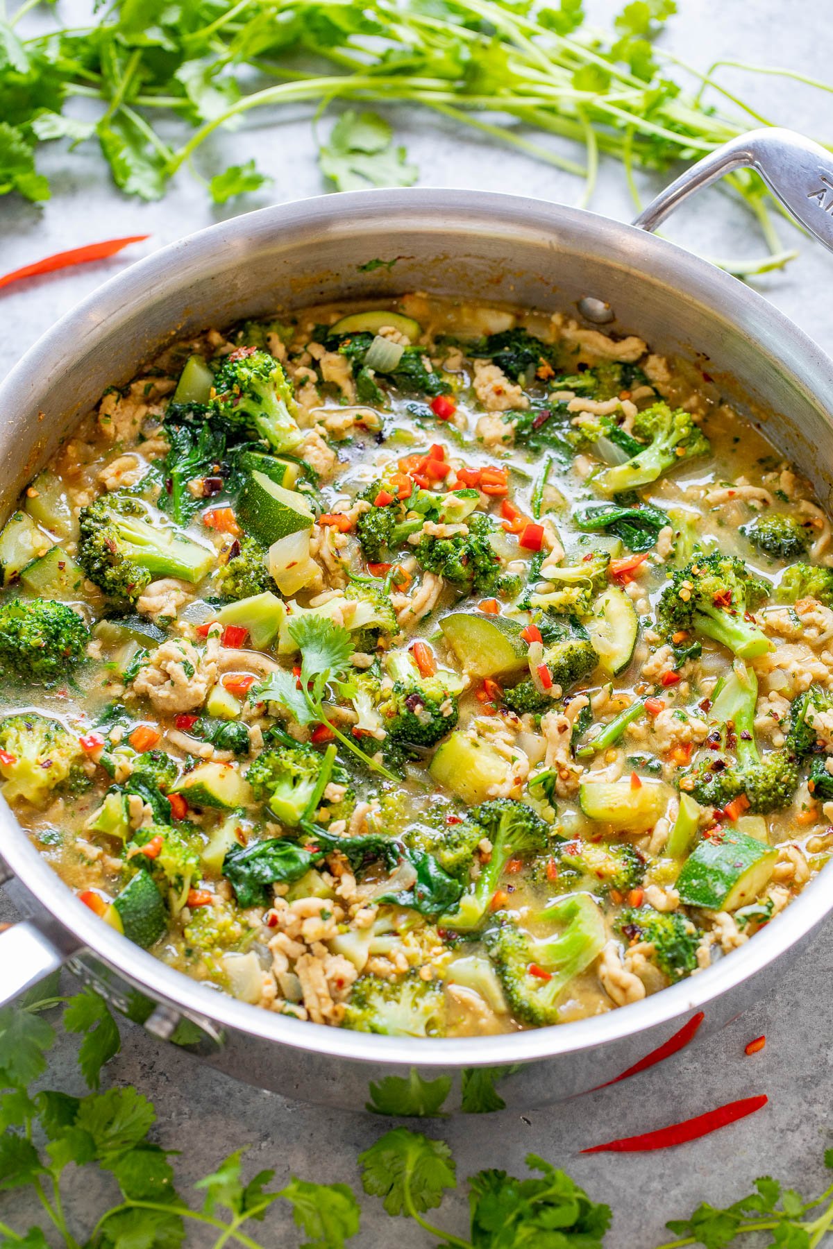 A skillet filled with a colorful, spicy chicken and vegetable green coconut curry garnished with fresh herbs.