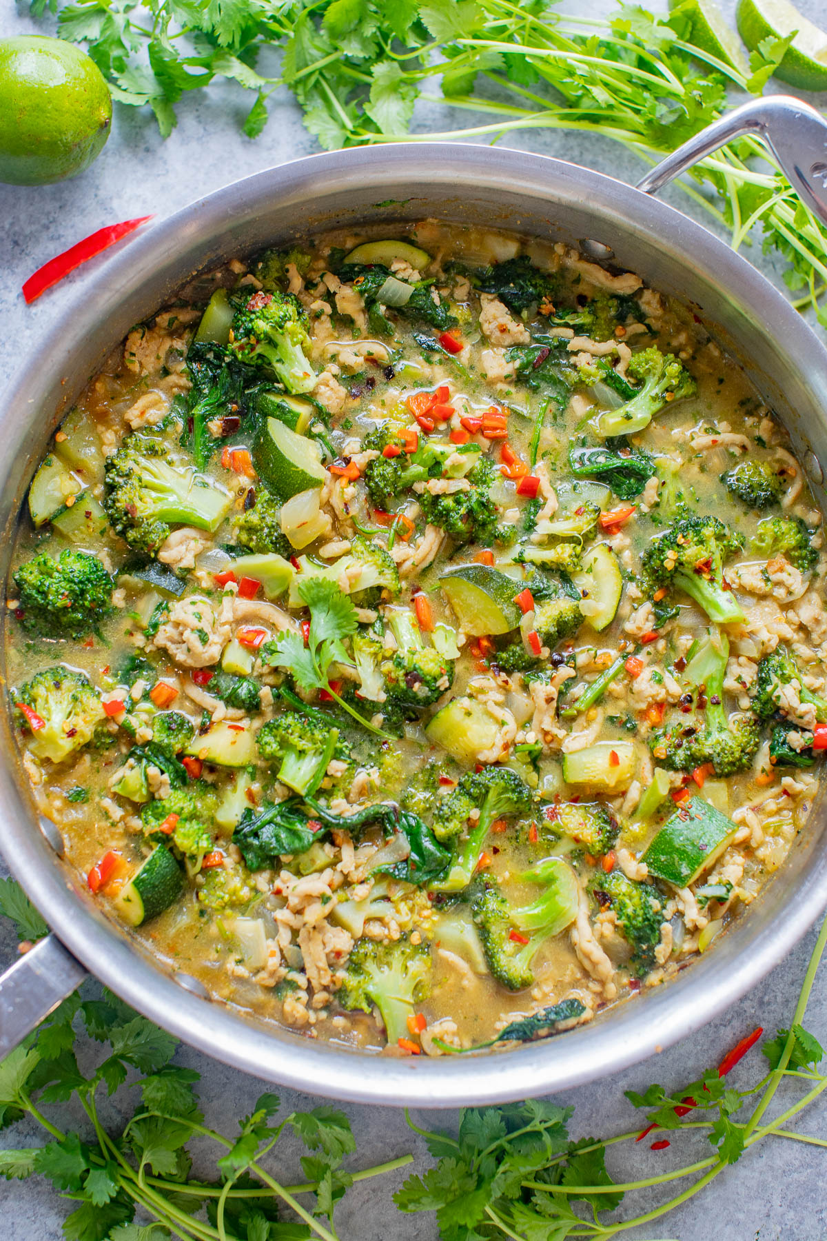 A pot of green curry with broccoli, zucchini, and red peppers.
