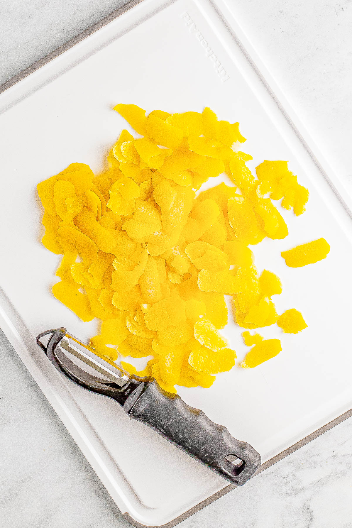 Lemon peels on a white cutting board with a metal peeler.
