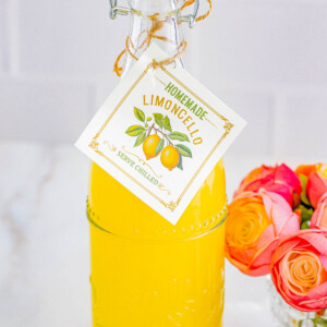 A bottle of homemade limoncello with a descriptive tag, next to a bouquet of roses.