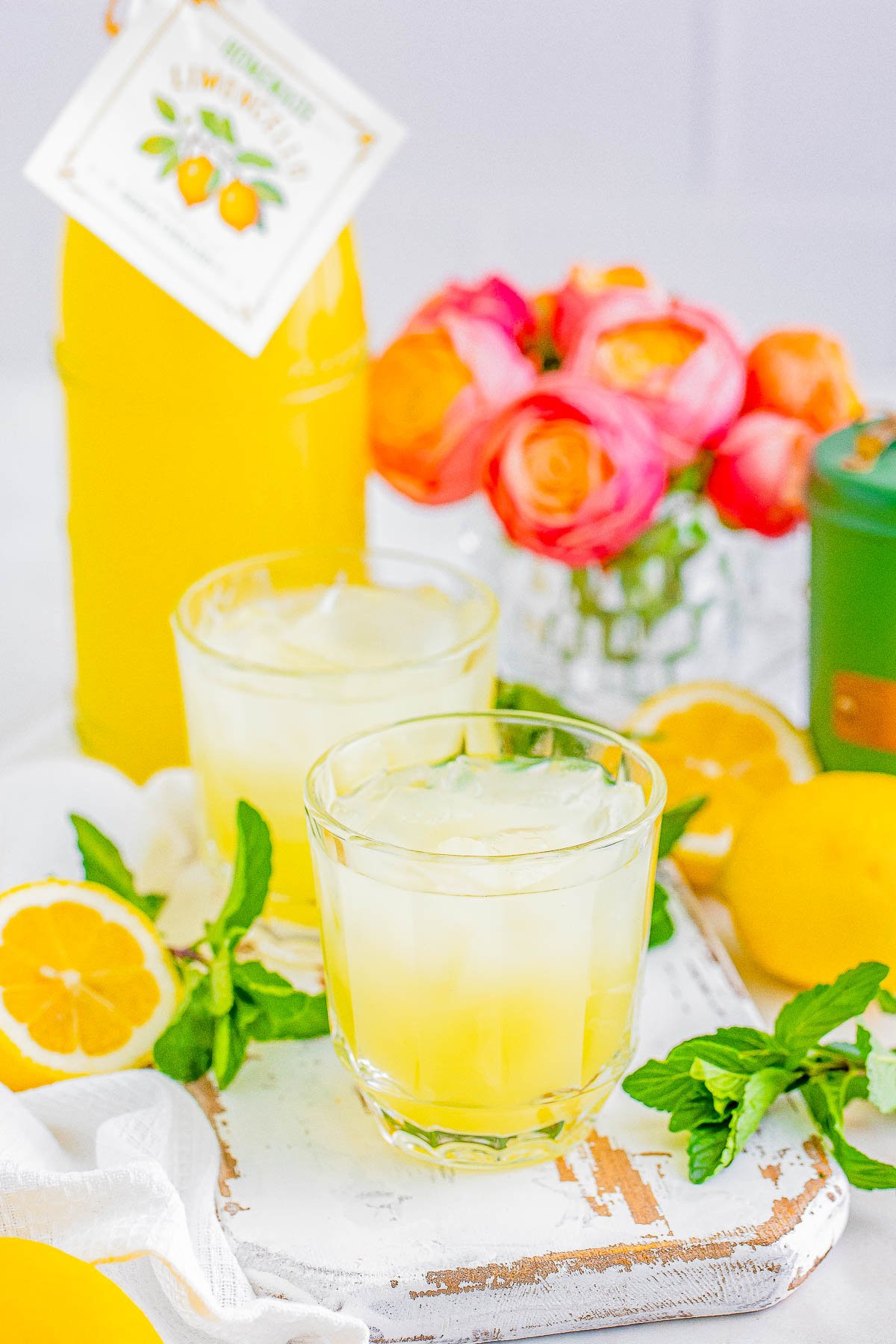 Glass of limoncello with fresh lemons, mint, and a backdrop of limoncello and flowers.