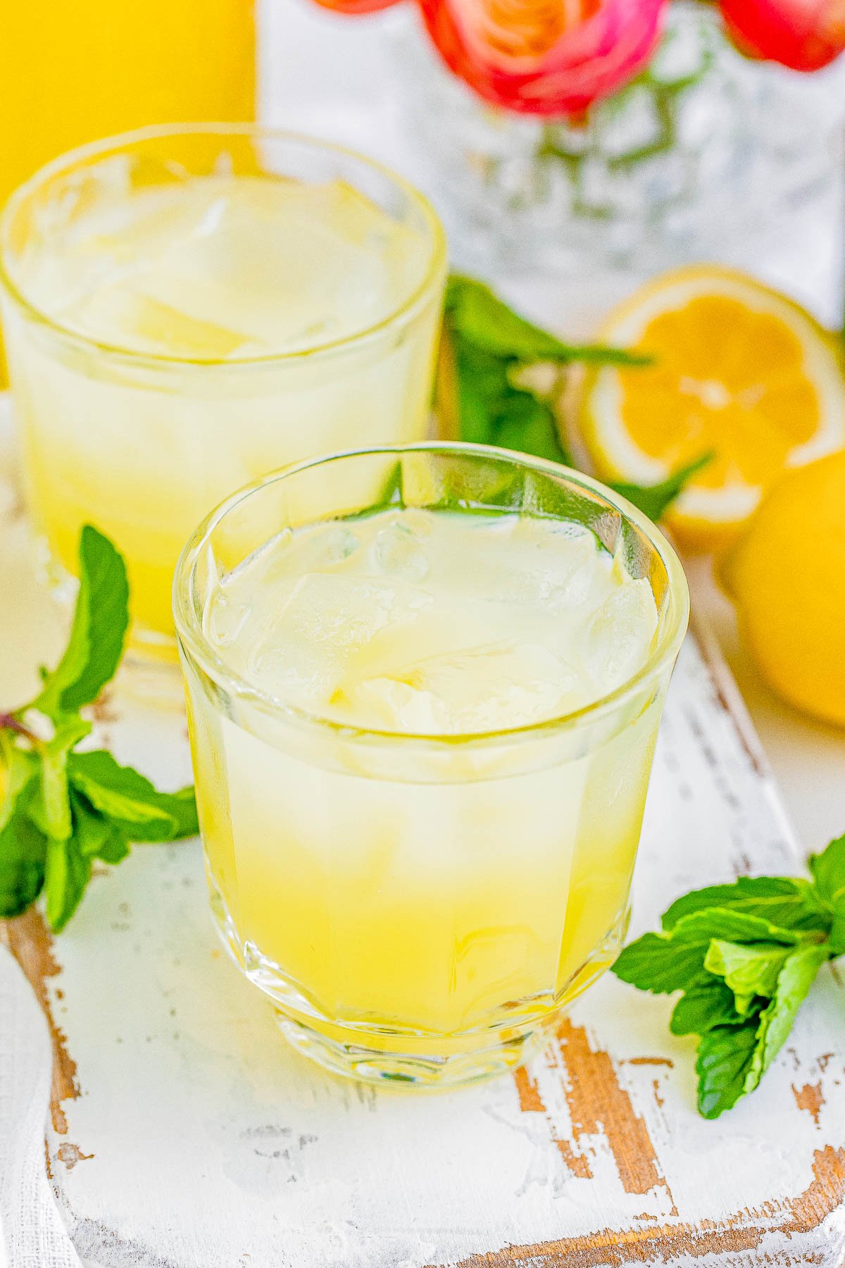 Two glasses of limoncello with ice, surrounded by fresh lemons and mint leaves on a rustic table.