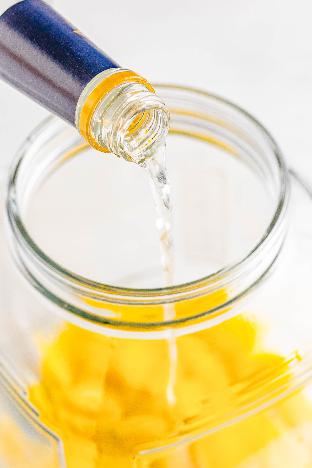 Pouring a clear liquid from a bottle into a glass jar filled with lemon peels.
