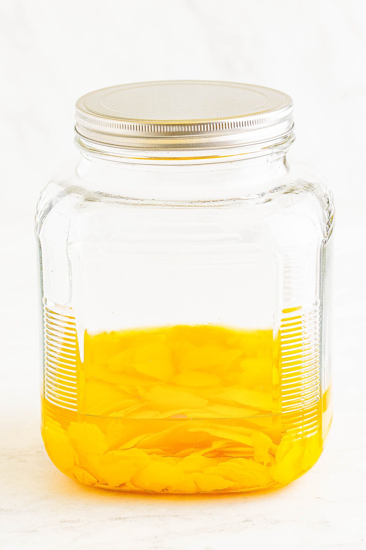 A glass jar with Everclear and lemon peels against a white background.