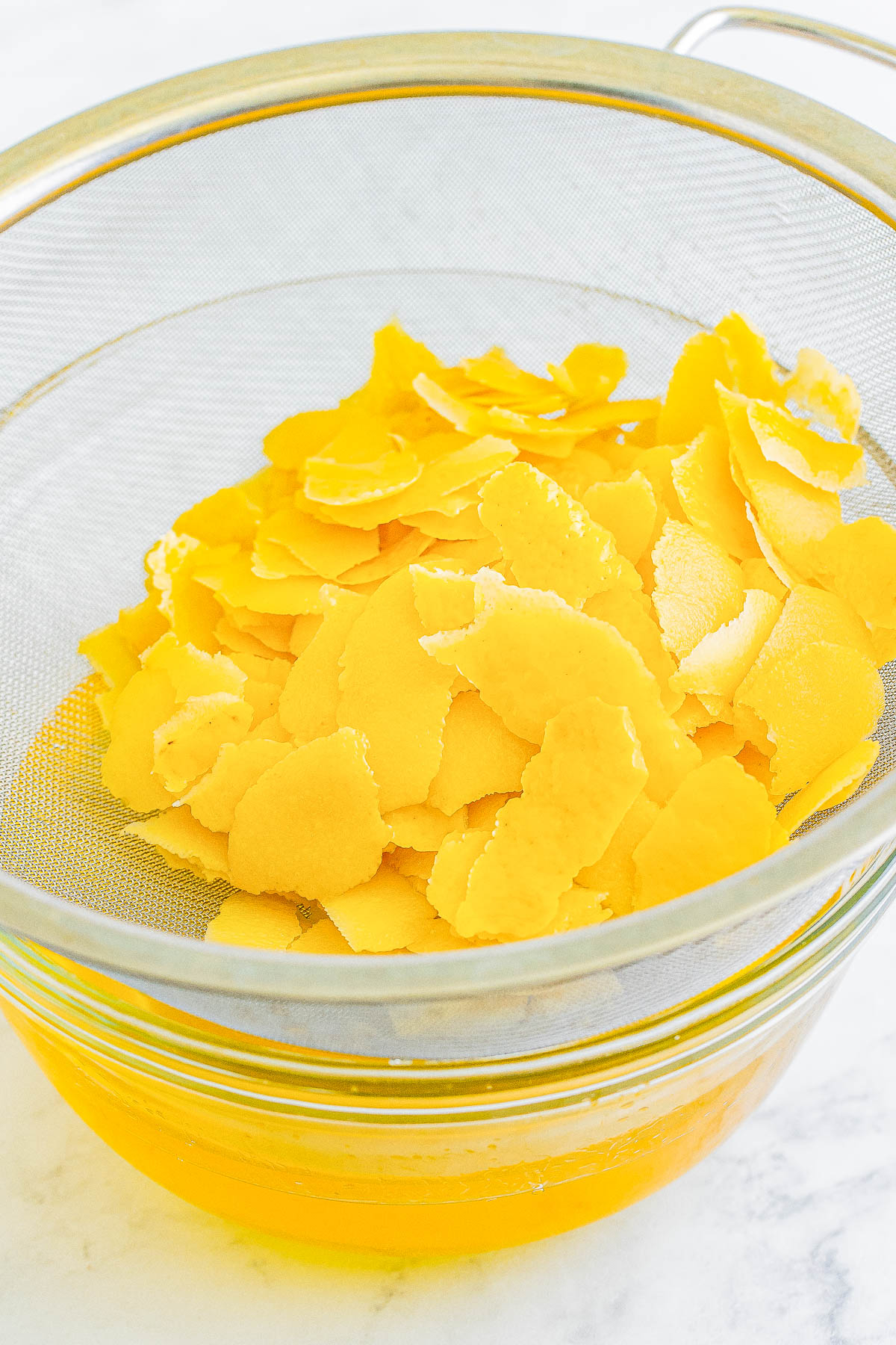 Lemon peels being strained in a sieve above a bowl to catch the juice.