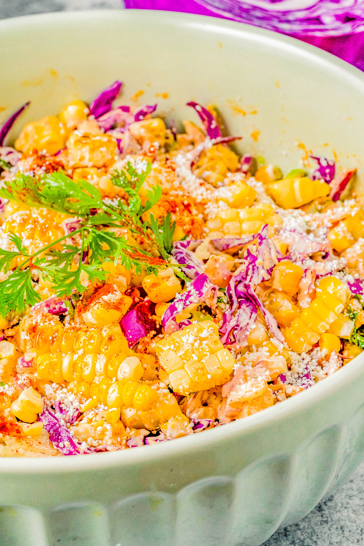 A vibrant bowl of salad with corn, red cabbage, herbs, and grated cheese, served in a white dish.