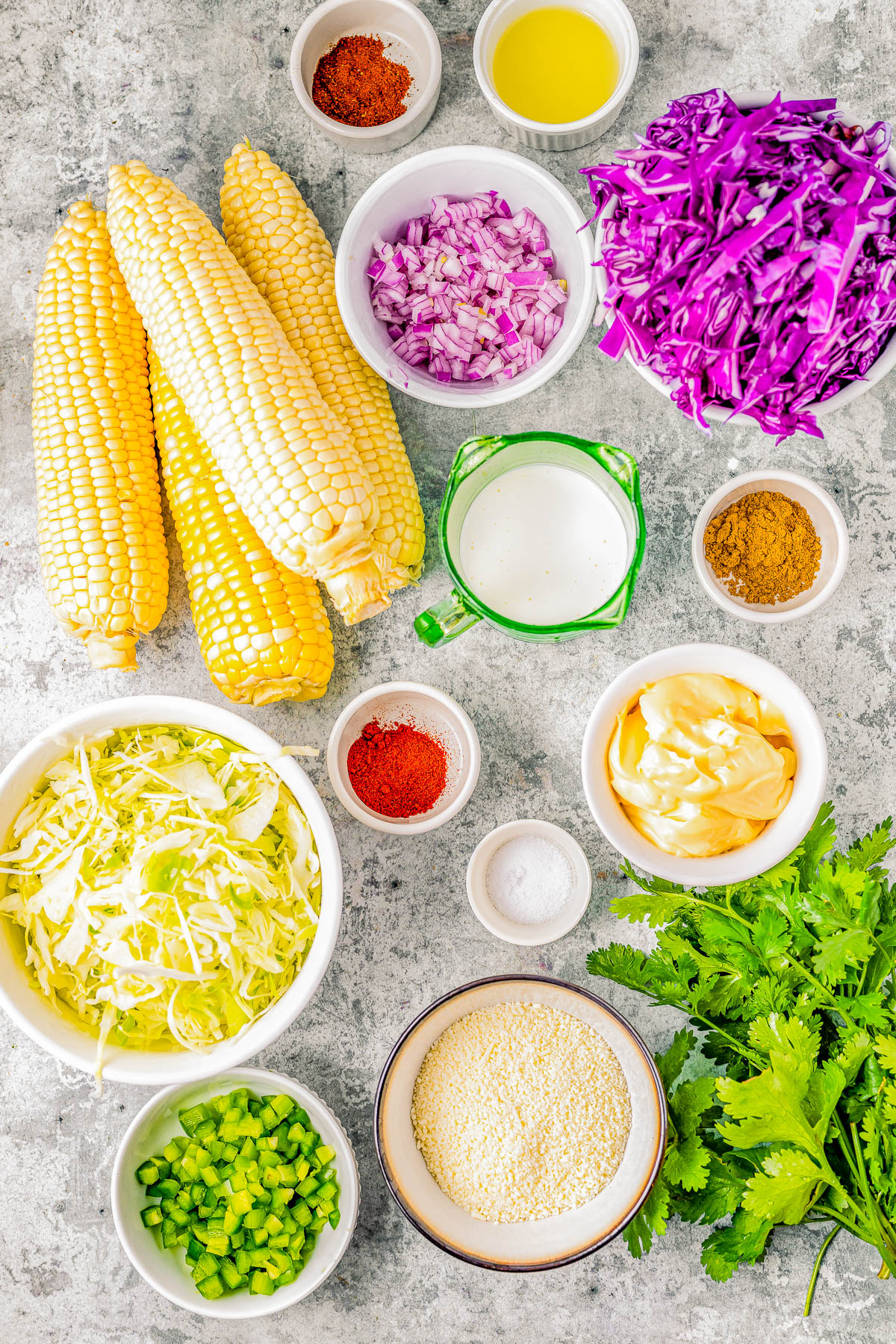 Various fresh ingredients for cooking displayed on a kitchen surface, including corn, purple cabbage, onions, herbs, spices, and oils.
