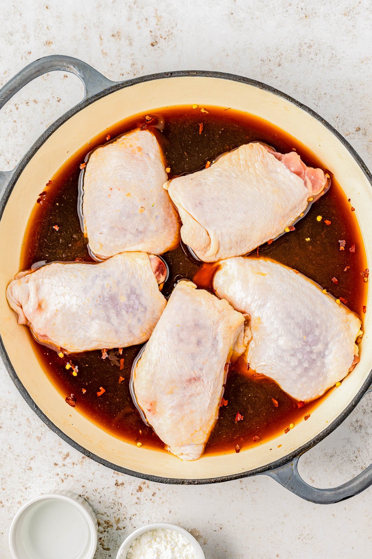 Raw chicken thighs marinating in a spiced sauce in a large pan, viewed from above.