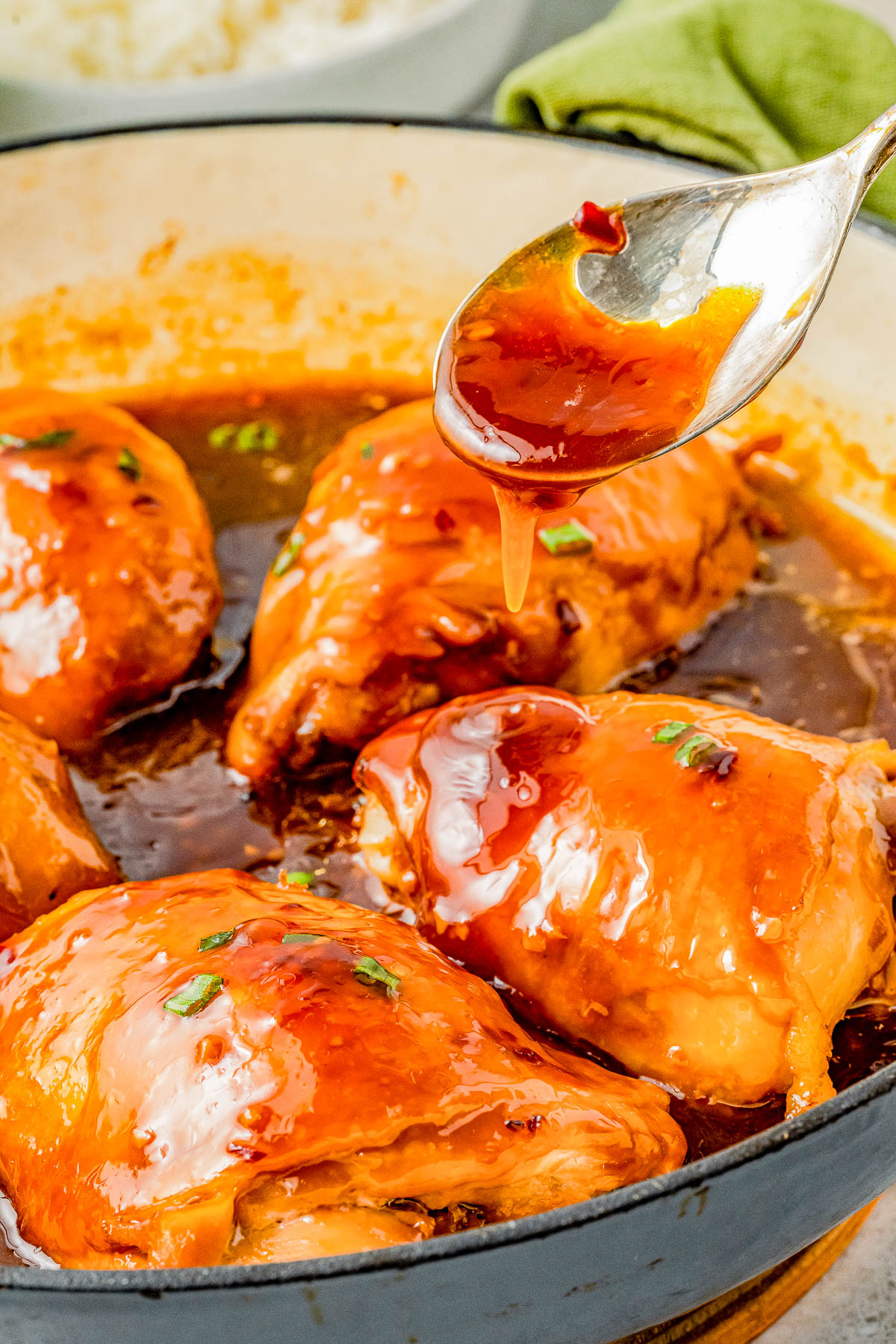 Spoon drizzling sauce over chicken breasts in a skillet, highlighting the shiny, savory glaze and sprinkled herbs.