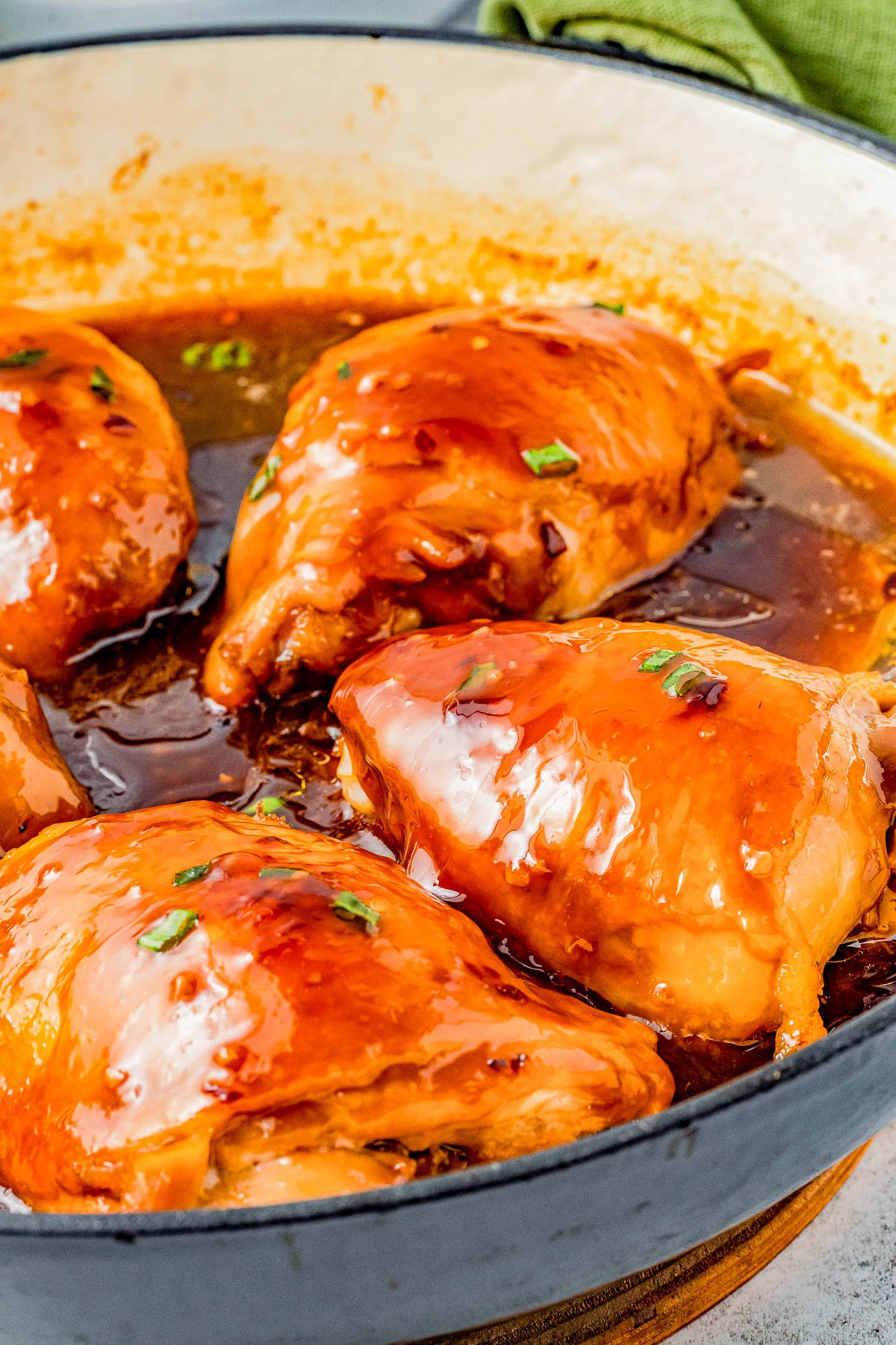 Five chicken breasts covered in shoyu sauce in a white cooking pot, garnished with chopped herbs.