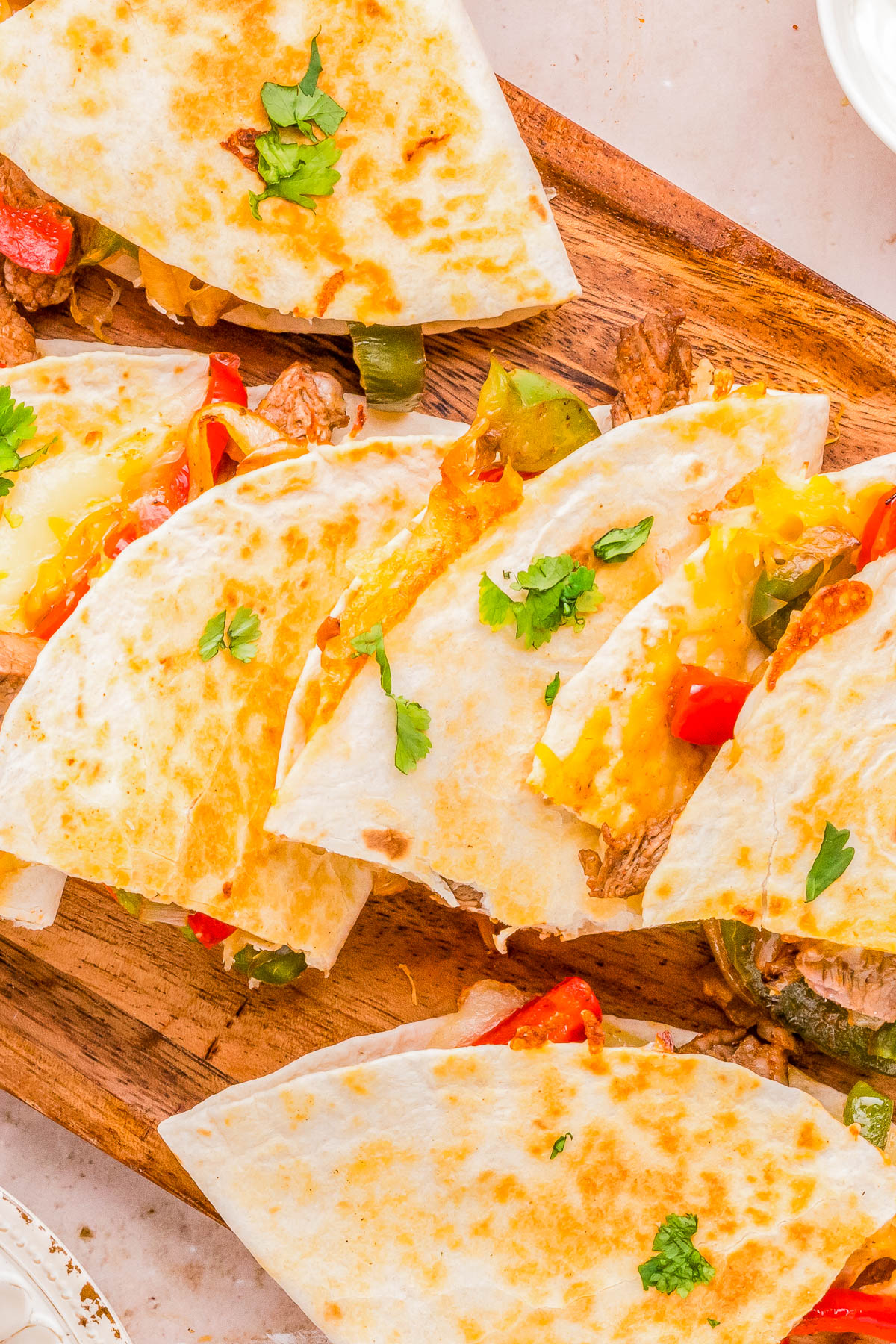 Sliced steak and cheese quesadillas with bell peppers and cilantro on a wooden board.