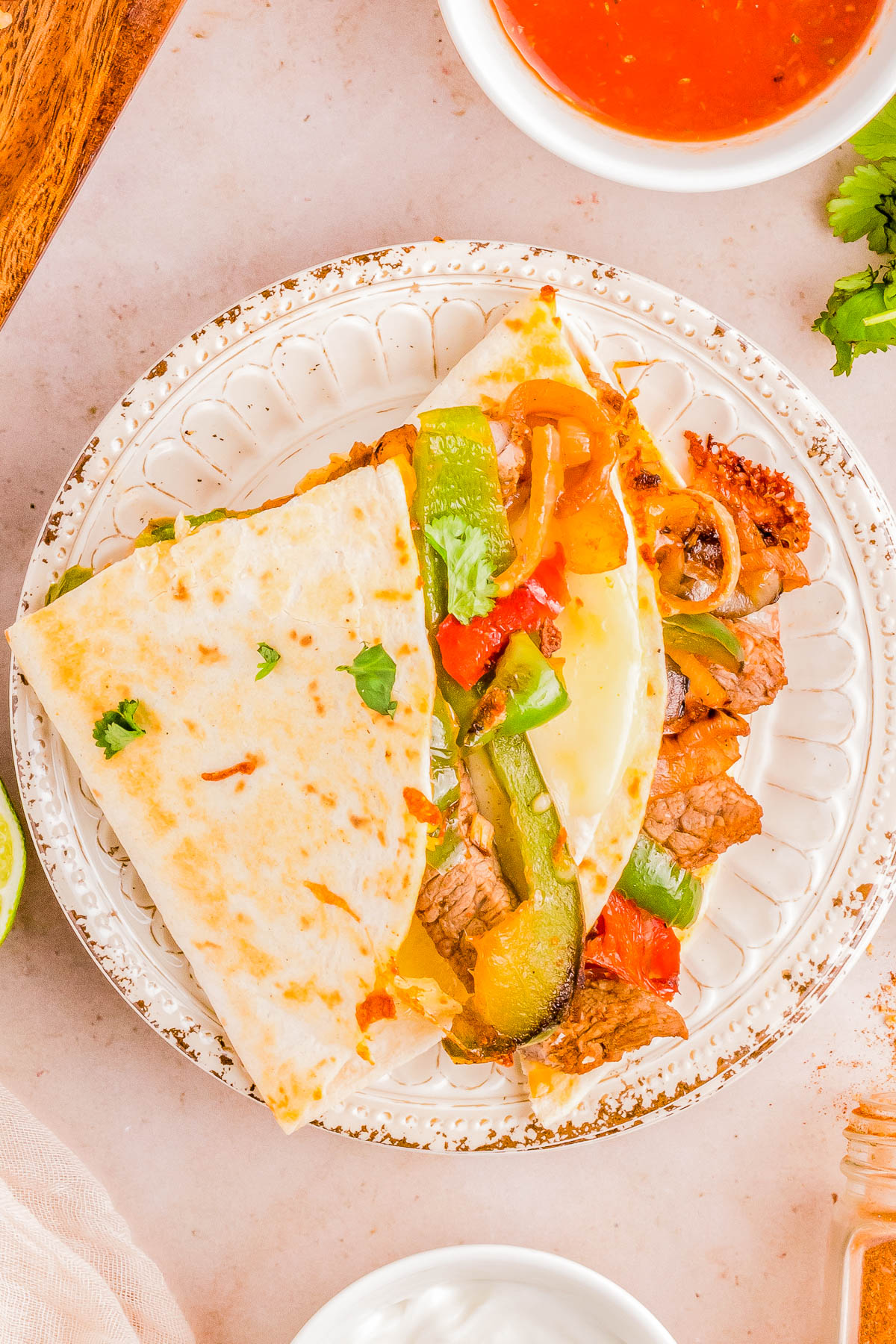 A plate with a half-folded quesadilla filled with beef, bell peppers, and melted cheese, served next to a bowl of salsa.