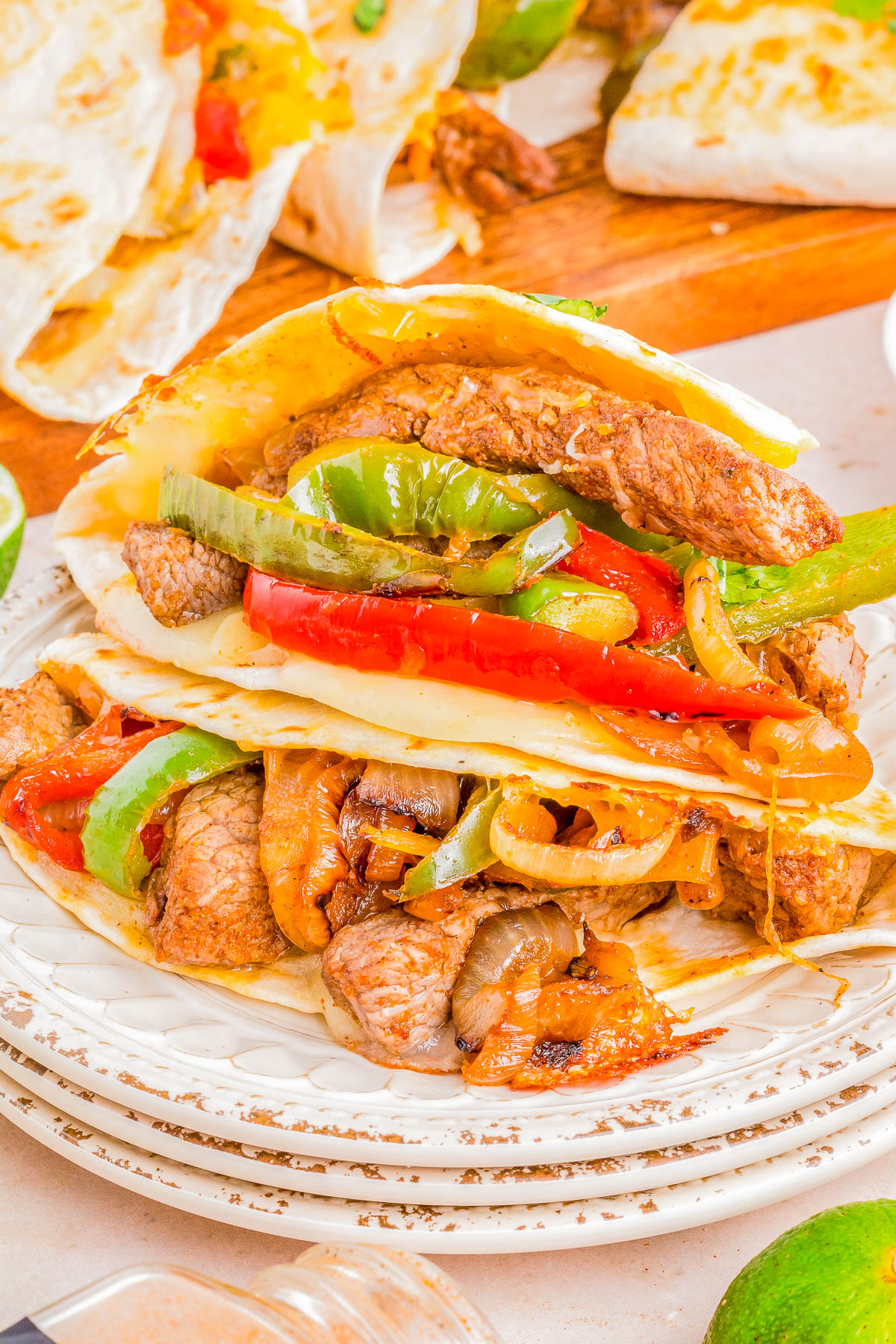 A close-up image of a steak quesadillas with colorful bell peppers, onions, and melted cheese in a soft tortilla, served on a white plate.