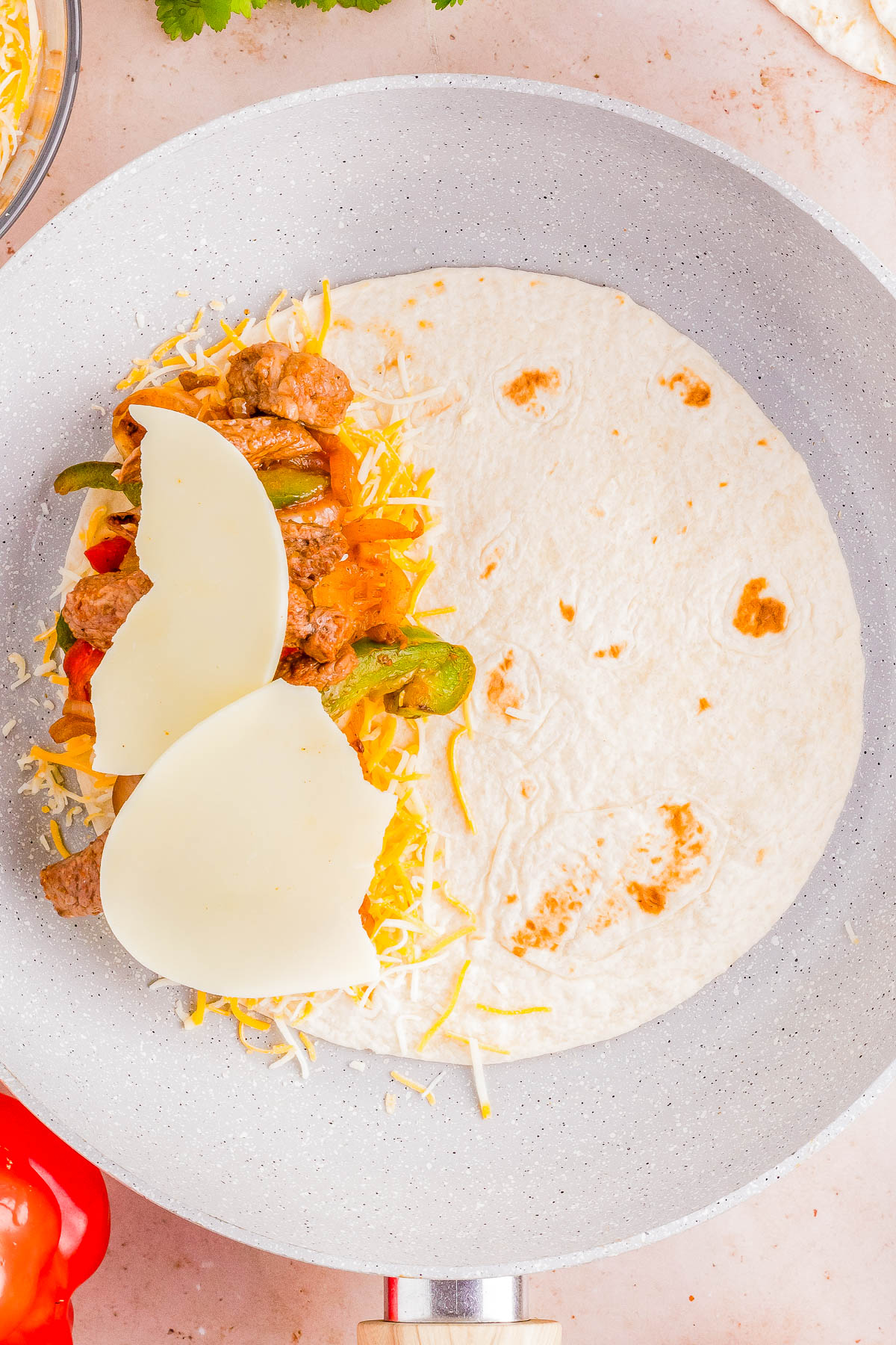 A tortilla with cheese, sliced bell peppers, and ground meat on a plate, ready for assembly.
