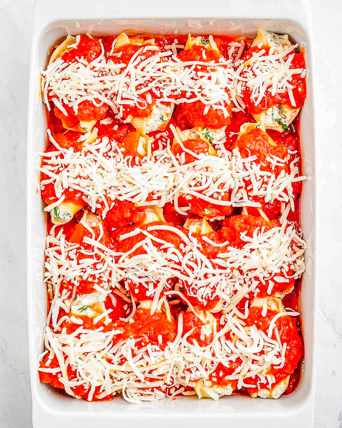 Unbaked stuffed shells in a dish, ready for the oven, topped with sauce and shredded cheese.