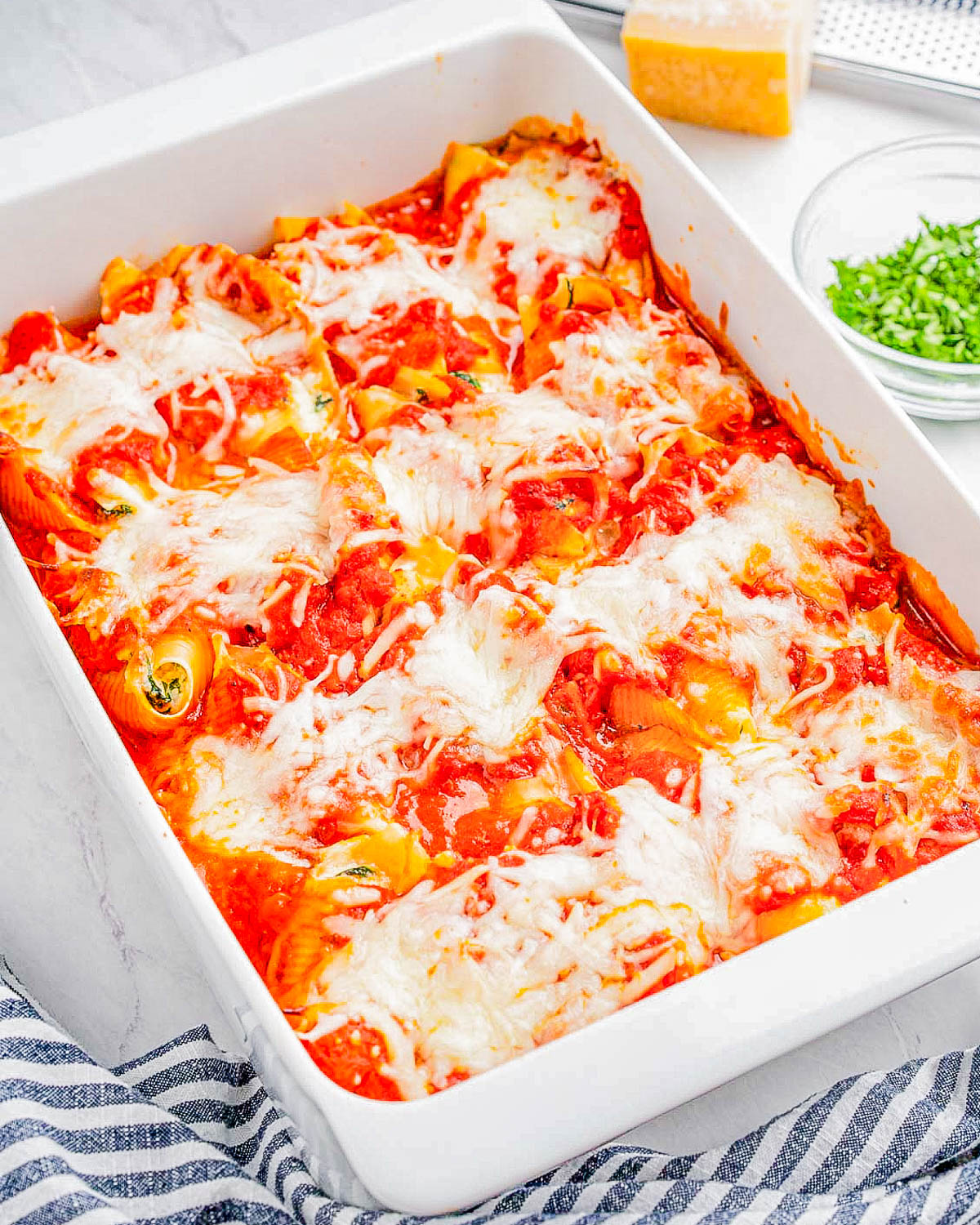 A dish of baked stuffed shells with melted cheese and tomato sauce in a white casserole.