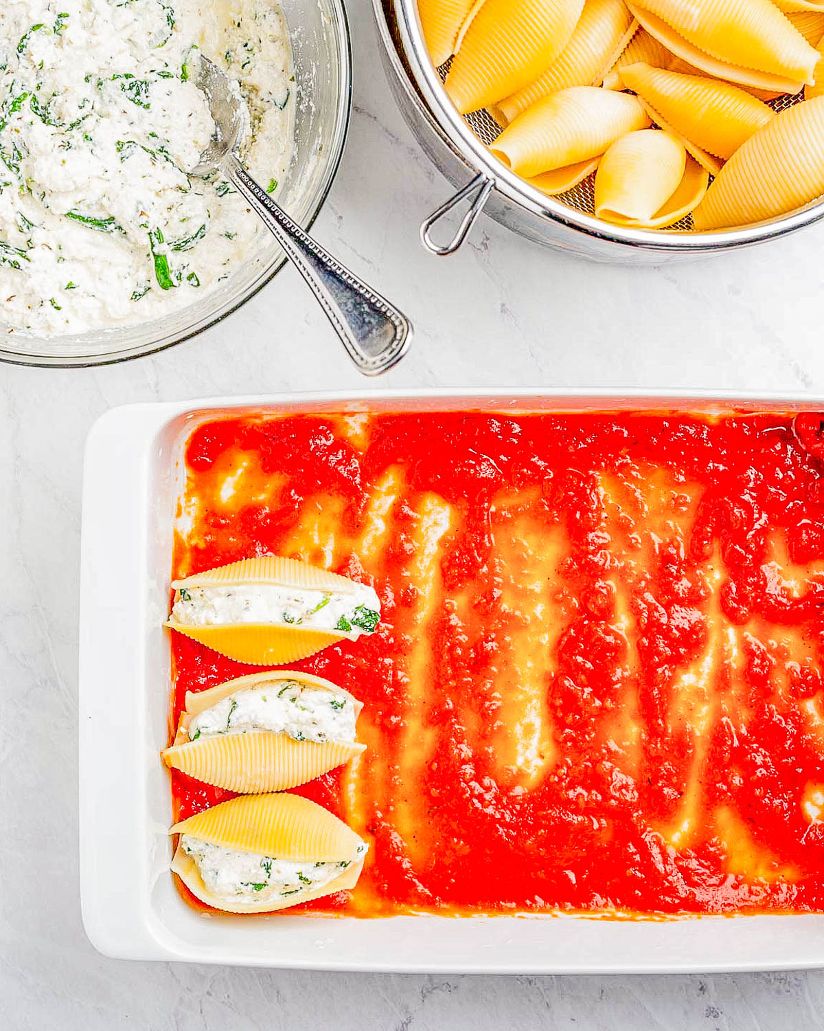 Preparation of stuffed pasta shells with ricotta filling and tomato sauce.