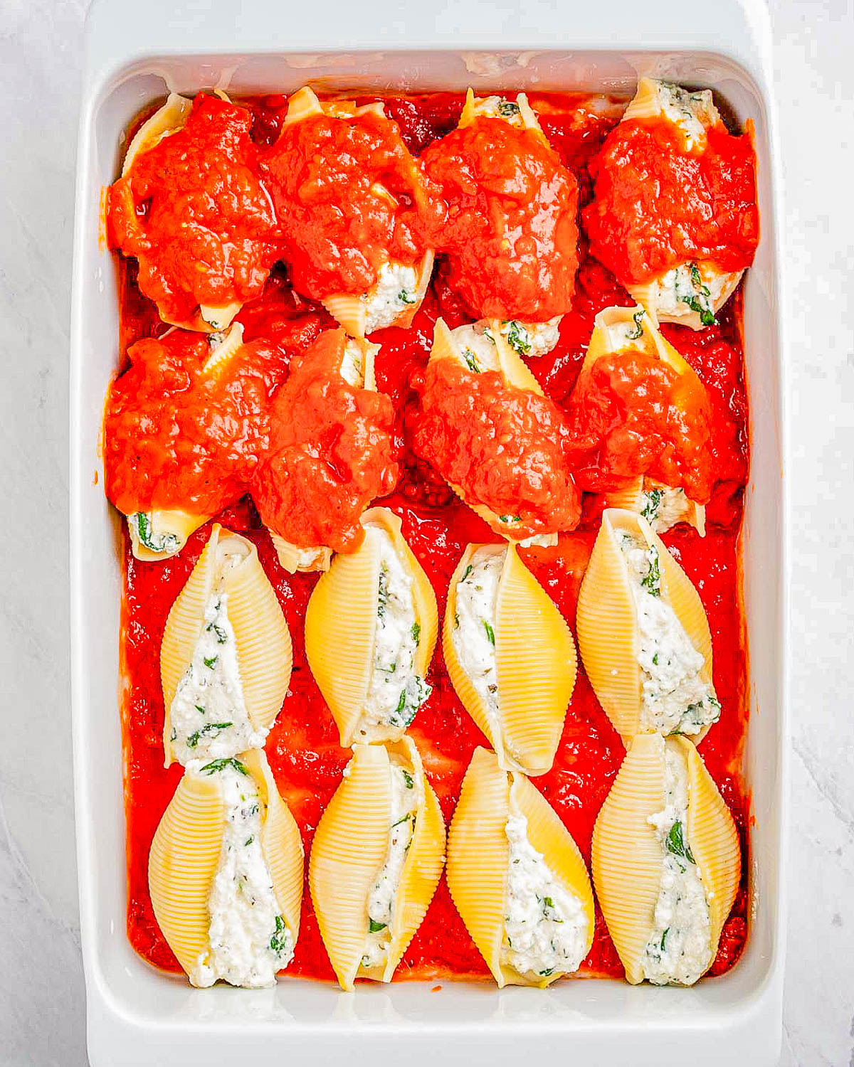 Stuffed jumbo pasta shells with ricotta cheese in a baking dish, topped with tomato sauce.