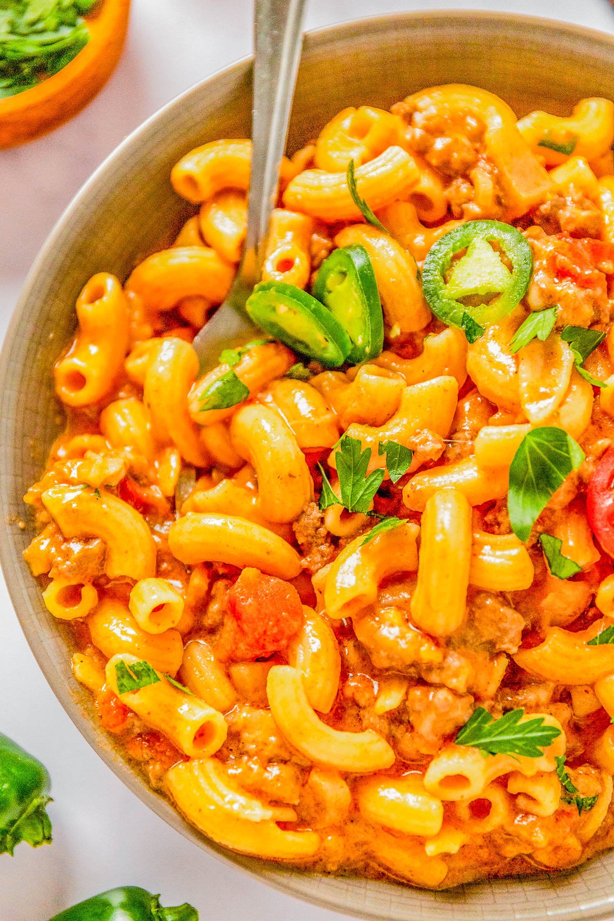 A bowl of macaroni pasta with tomato sauce, ground meat, sliced green bell peppers, and garnished with parsley.