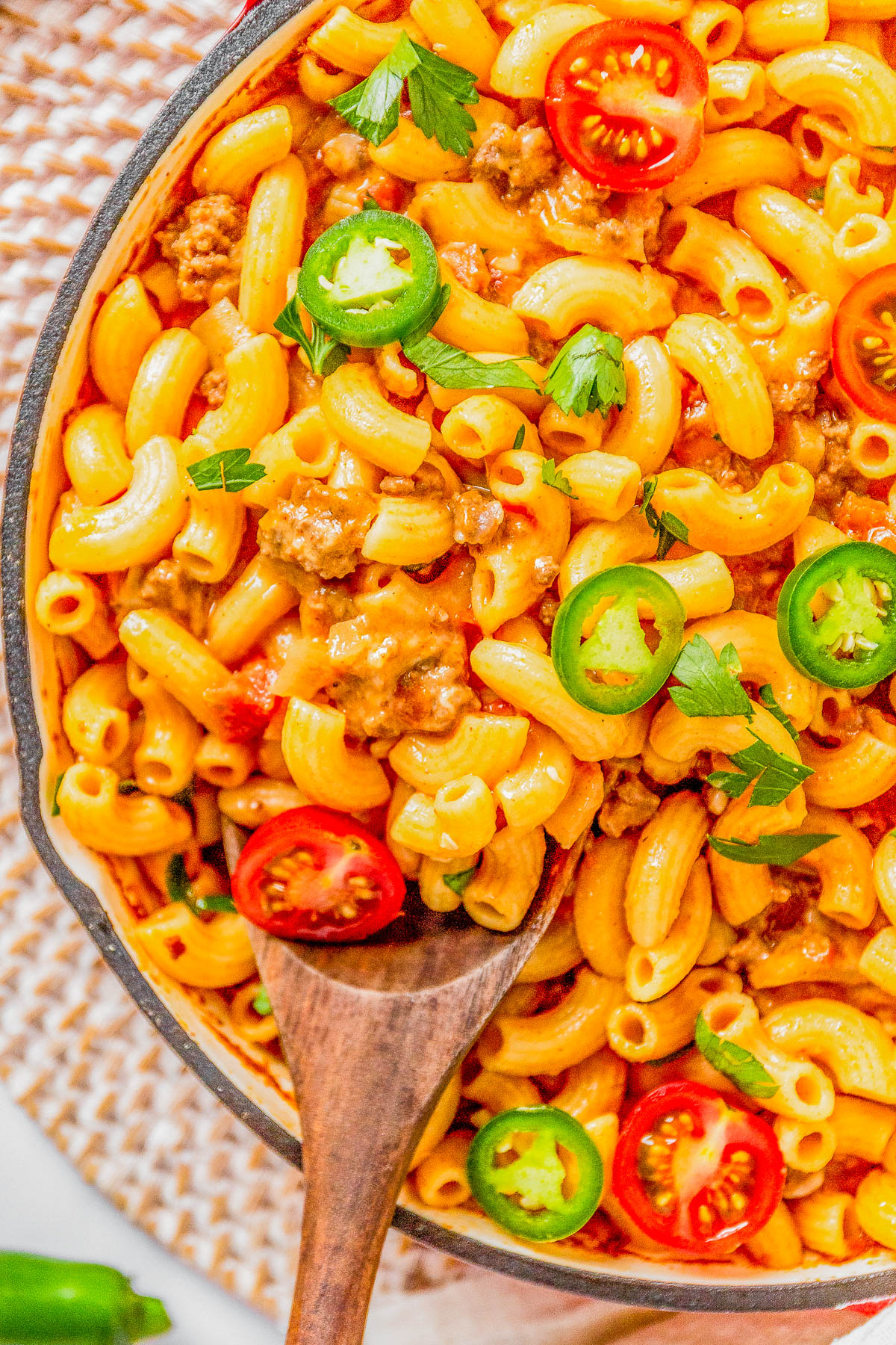 A skillet of cheesy macaroni with ground beef, garnished with sliced tomatoes, jalapeños, and fresh herbs.