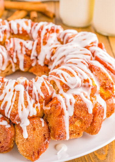 A freshly baked pull-apart bread topped with white icing on a white plate, accompanied by two glasses of milk in the background.