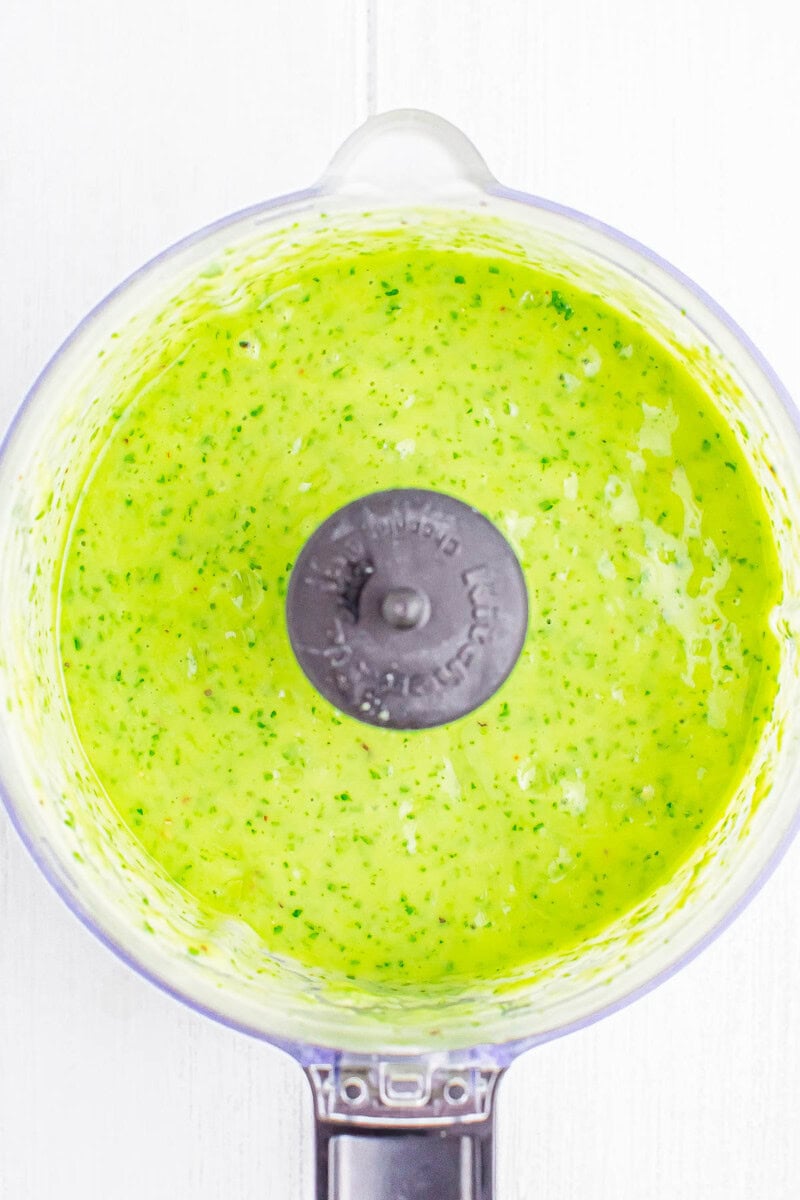 A food processor bowl containing a blended green sauce.