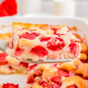 A slice of strawberry cobbler being lifted from a dish, showcasing ripe strawberries and a fluffy texture, with a glass of milk in the background.