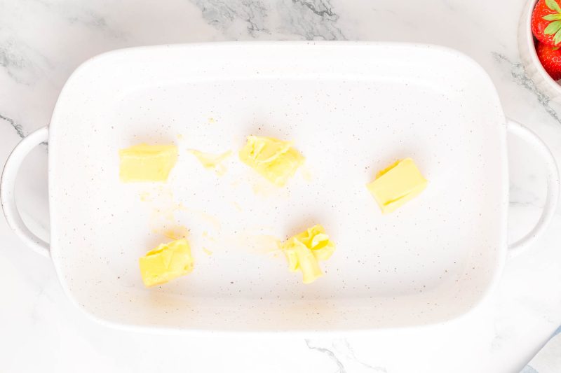 White ceramic baking dish on a marble surface containing several chunks of butter.
