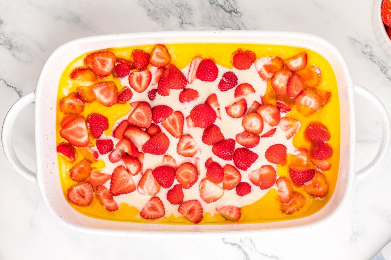 A dish of sliced strawberries on a bed of creamy custard in a white baking dish, viewed from above on a marble surface.