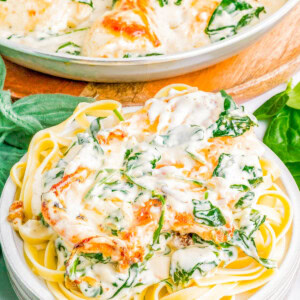 Plate of fettuccine pasta topped with a creamy spinach and cheese sauce, garnished with herbs. A serving dish of the same sauce is in the background.
