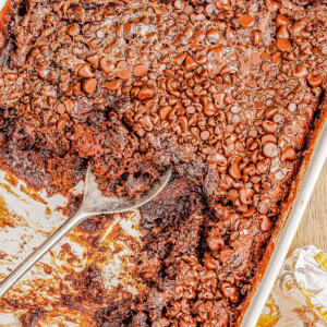 A baking dish filled with chocolate molten lava cake, topped with melted chocolate chips, partially scooped out with a large spoon.