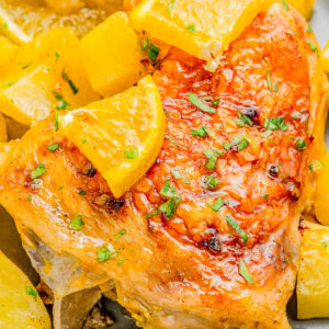 Roasted chicken with crispy skin, garnished with lemon slices and herbs, surrounded by roasted potato chunks.