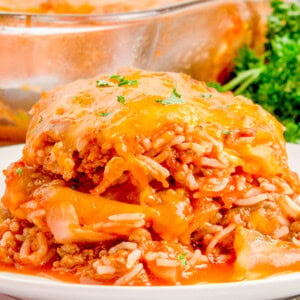 Close-up of a plate with a serving of cheesy beef and rice casserole, garnished with parsley. A glass baking dish with more casserole is visible in the background.