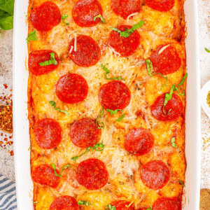 A baked pepperoni pizza casserole in a rectangular dish, topped with melted cheese and fresh basil.