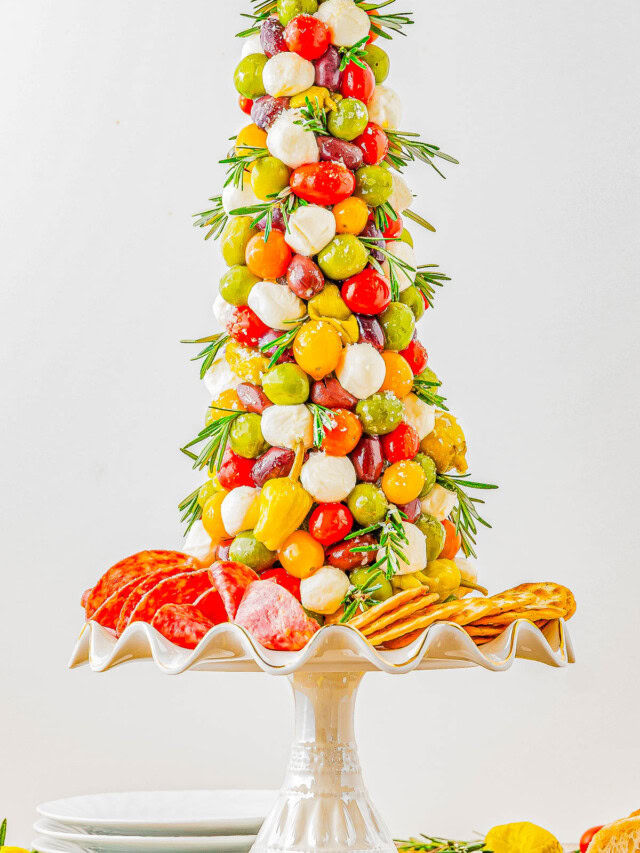 A tree-shaped appetizer display featuring grape tomatoes, mozzarella balls, olives, and peppers on skewers, garnished with rosemary, with salami and crackers at the base on a pedestal stand.