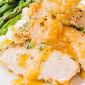 Sliced turkey breast with gravy on a white plate, served with mashed potatoes and asparagus.