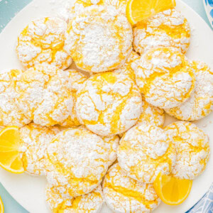 A plate of lemon crinkle cookies dusted with powdered sugar, garnished with lemon slices.
