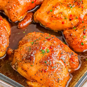 Close-up of four glazed and seasoned chicken thighs in a glass baking dish.