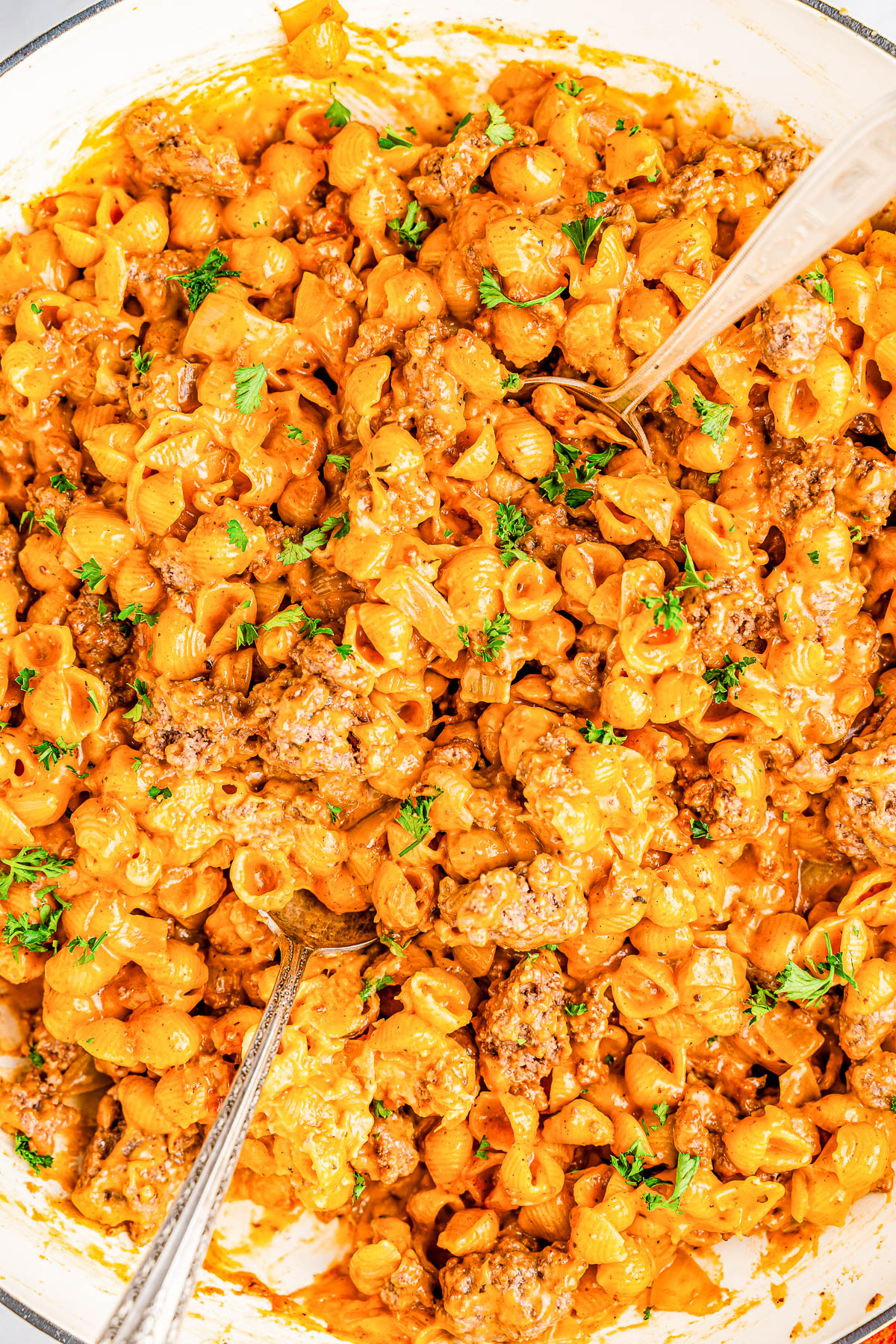 A close-up of creamy pasta shells mixed with ground meat and garnished with parsley, with two spoons for serving.