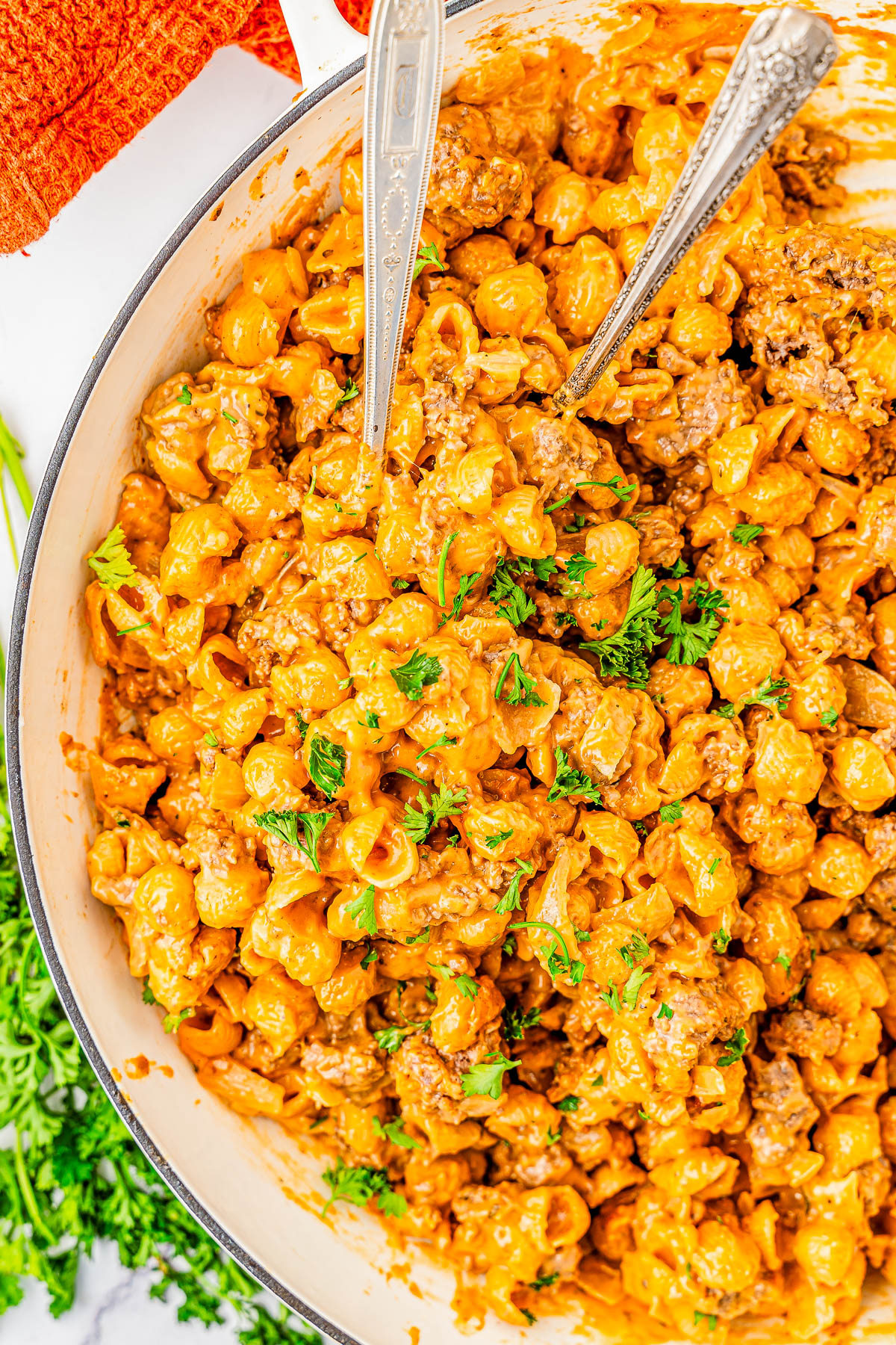 A dish of creamy pasta with ground meat, garnished with parsley. Two serving utensils are placed in the dish.