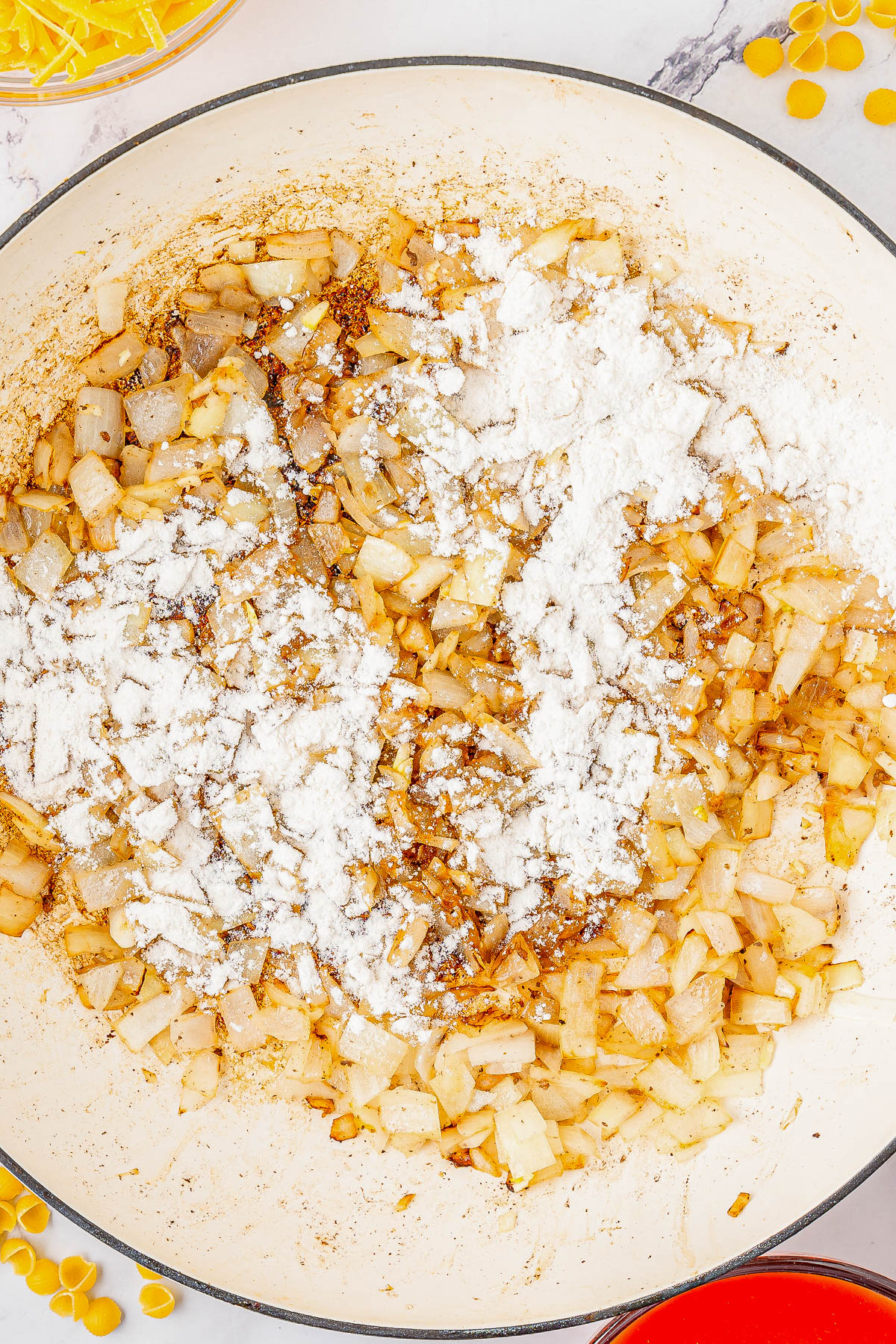 Chopped onions being sautéed in a pan with a coating of white flour on top.
