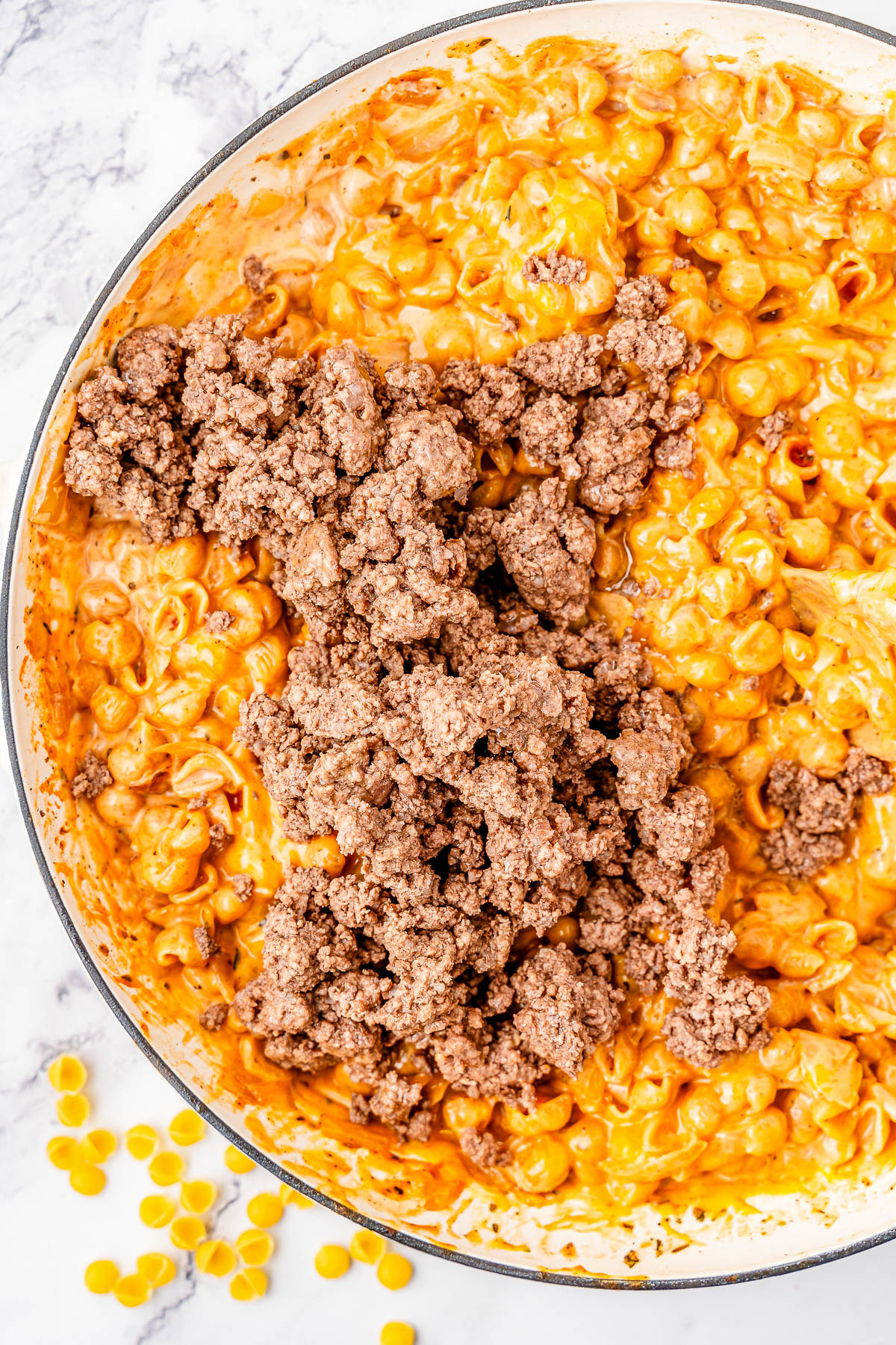 A pot of macaroni and cheese mixed with ground beef on a marble countertop.