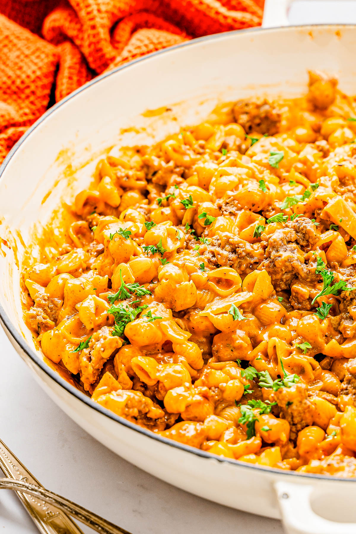 A skillet filled with cheesy pasta shells and ground meat, garnished with fresh parsley.