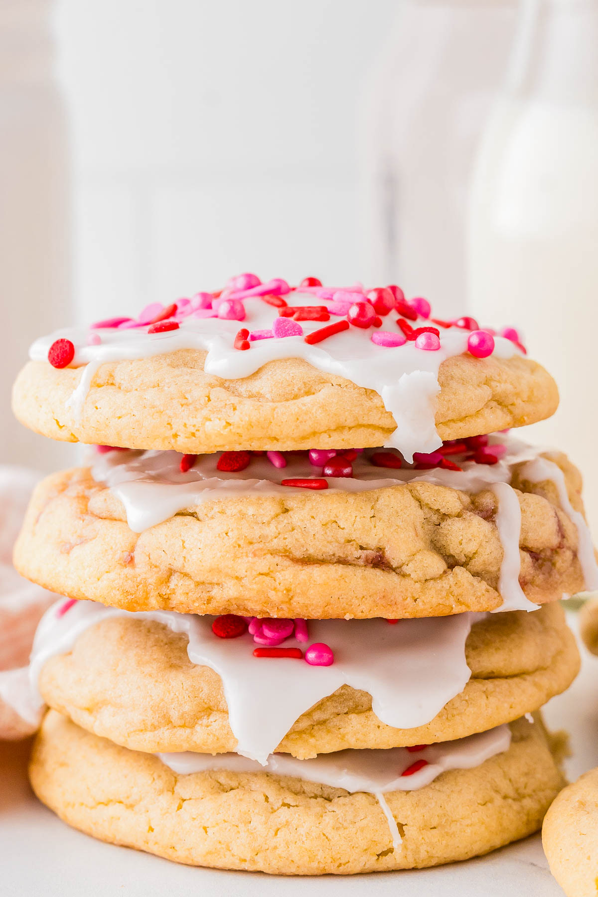 A stack of three cookies with white icing and pink and red sprinkles.