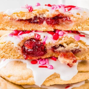 Stack of cookies with white icing and pink sprinkles, two halves on top showing a cherry filling.
