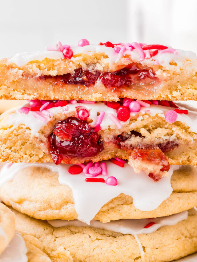 Stack of cookies with white icing and pink sprinkles, two halves on top showing a cherry filling.