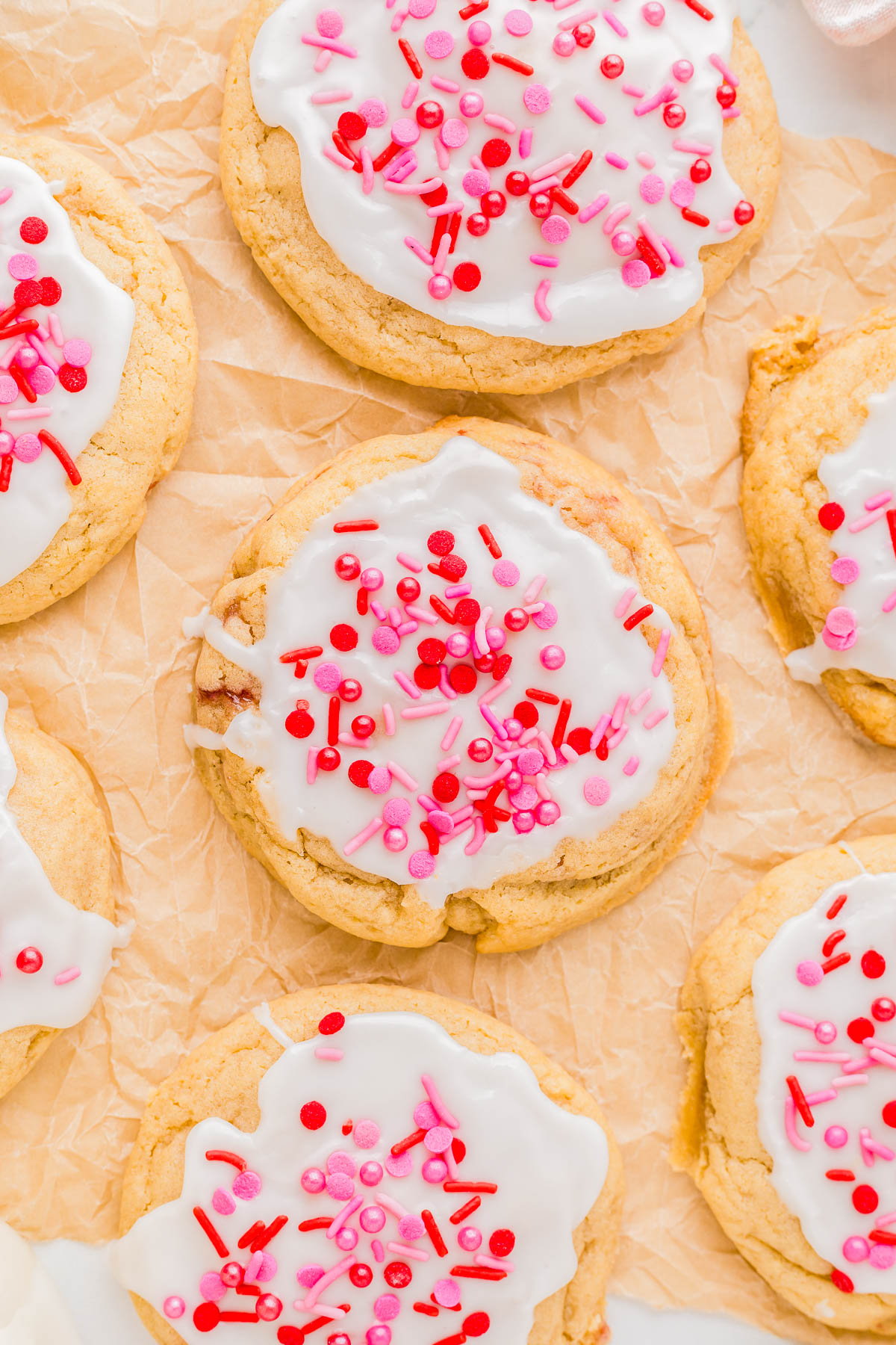 Cookies with white icing and pink and red sprinkles on a sheet of parchment paper.