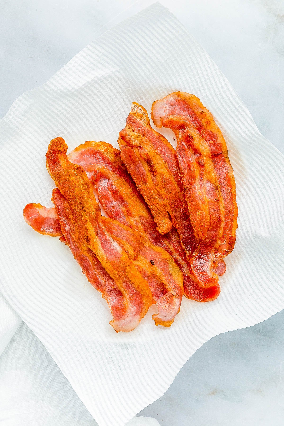 Crispy cooked bacon strips arranged on a white paper towel.